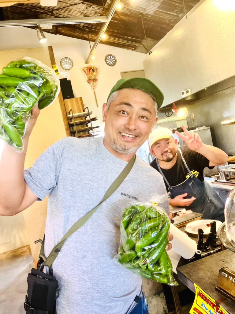 生鮮野菜清水商店代表の清水さんが、配達先:DAKOTA RUSTIC TABLEのオーナーと笑顔で映る画像。